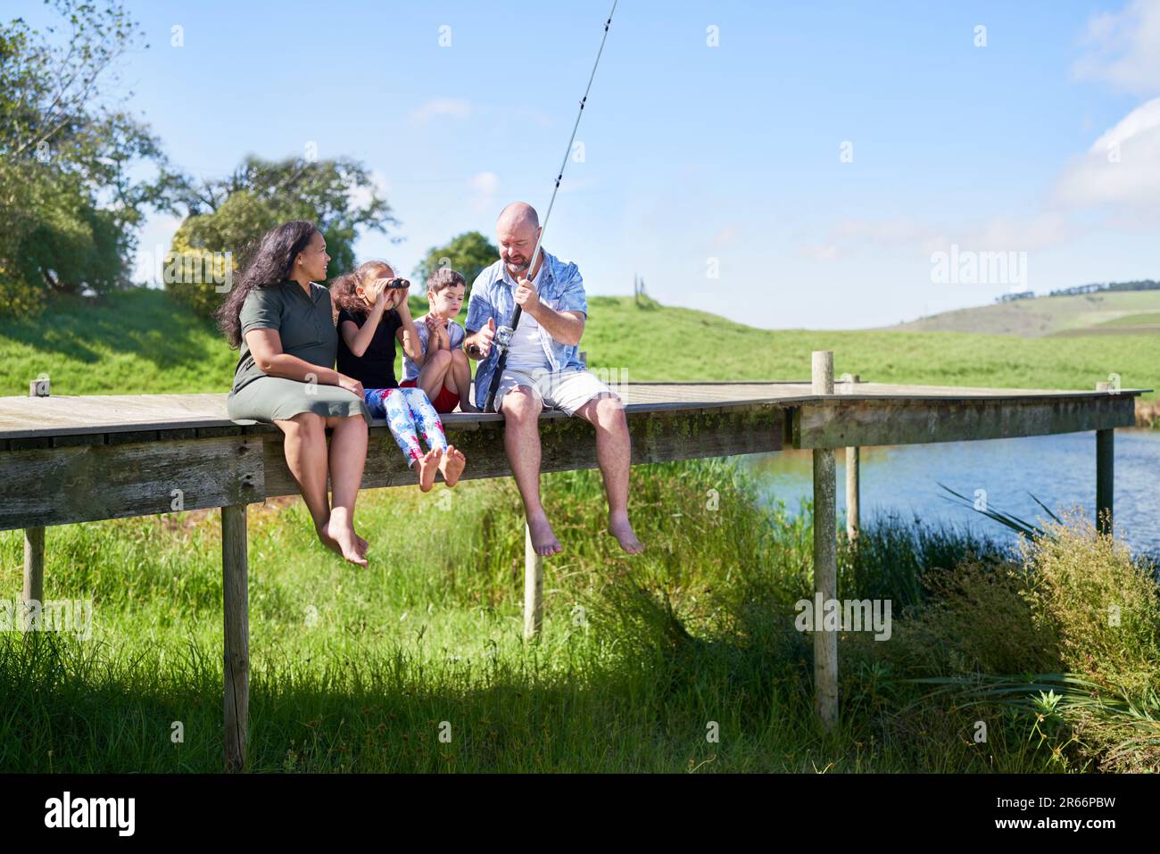 Family with binoculars fishing on pier at summer lakeside Stock Photo