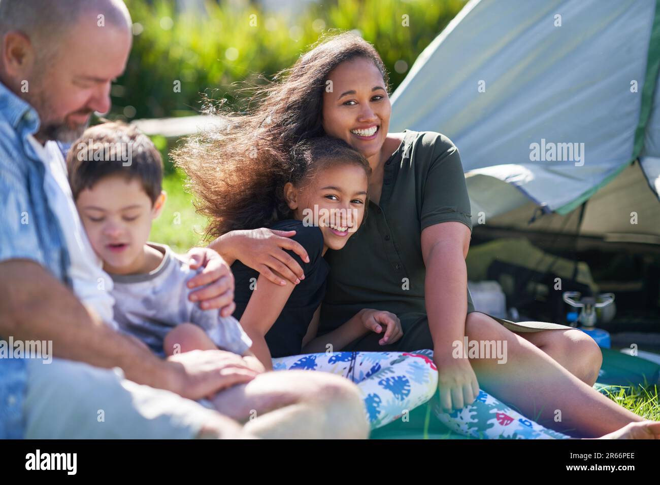 Portrait happy family hugging outside tent at summer campsite Stock Photo