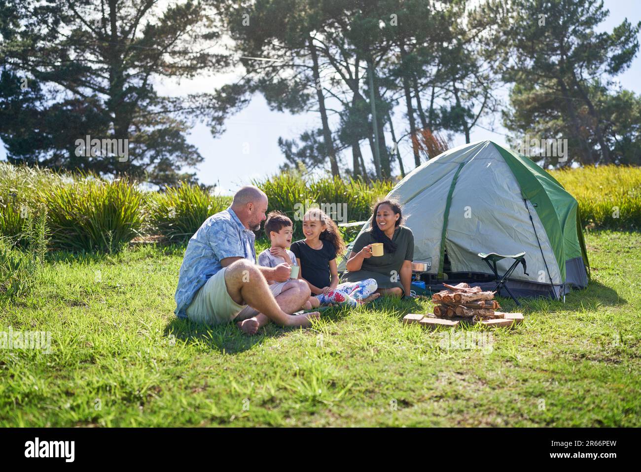 Happy family talking and drinking outside tent at sunny summer campsite Stock Photo