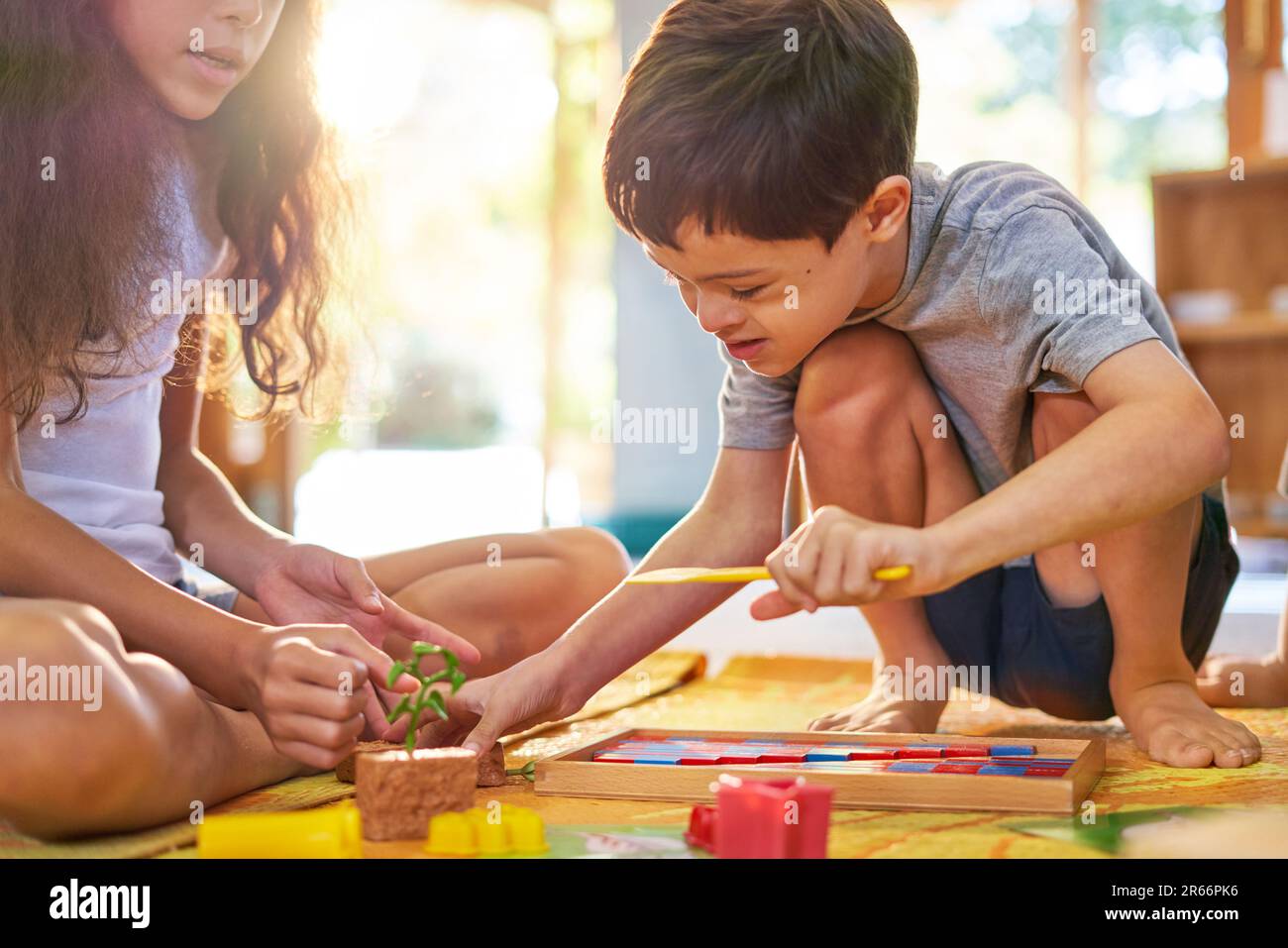 Sister watching brother with Down Syndrome playing with toys on floor Stock Photo