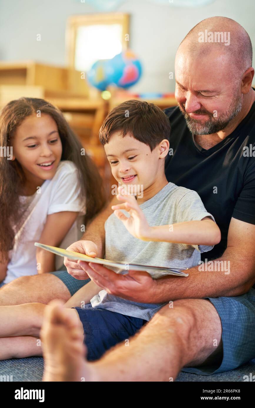 Cute boy with Down Syndrome reading book with family at home Stock Photo