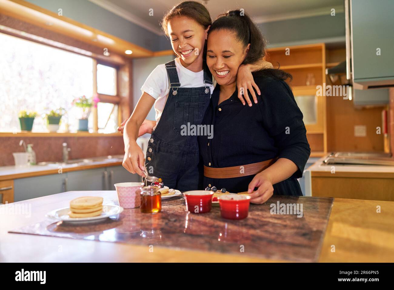 Happy mother and daughter eating pancakes in morning kitchen Stock Photo