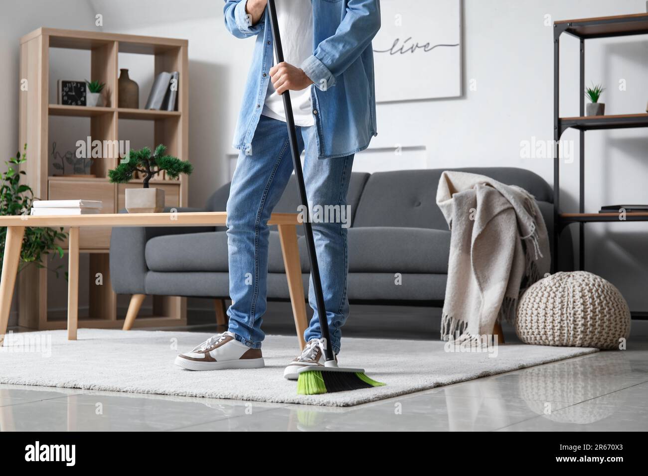 Young man sweeping carpet with broom at home Stock Photo