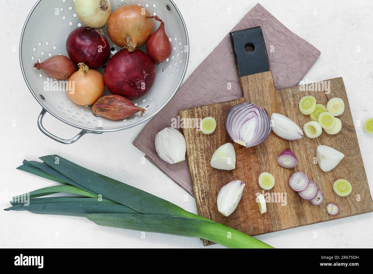 Wooden board and colander with different kinds of onion on white ...