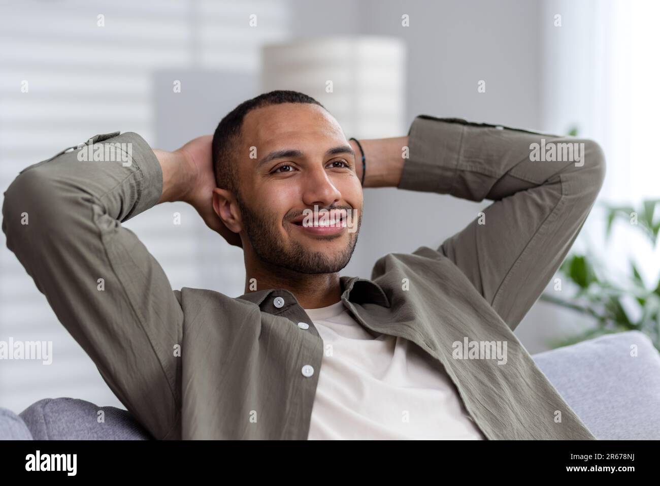 Portrait of a satisfied African American businessman, freelancer man sitting at home with his hands behind his head on the couch and resting after a h Stock Photo