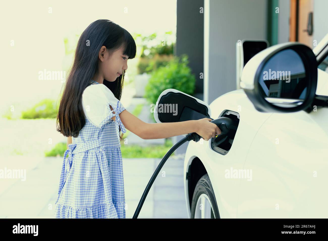 A playful girl holding an EV plug, a home charging station providing a
