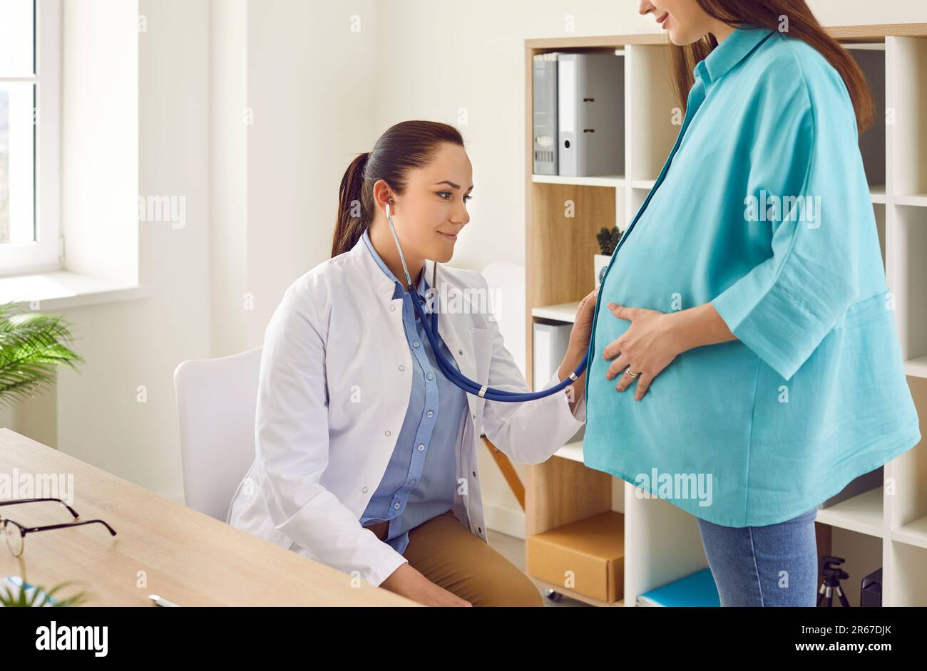 Doctor is using stethoscope to examine young pregnant woman and baby in