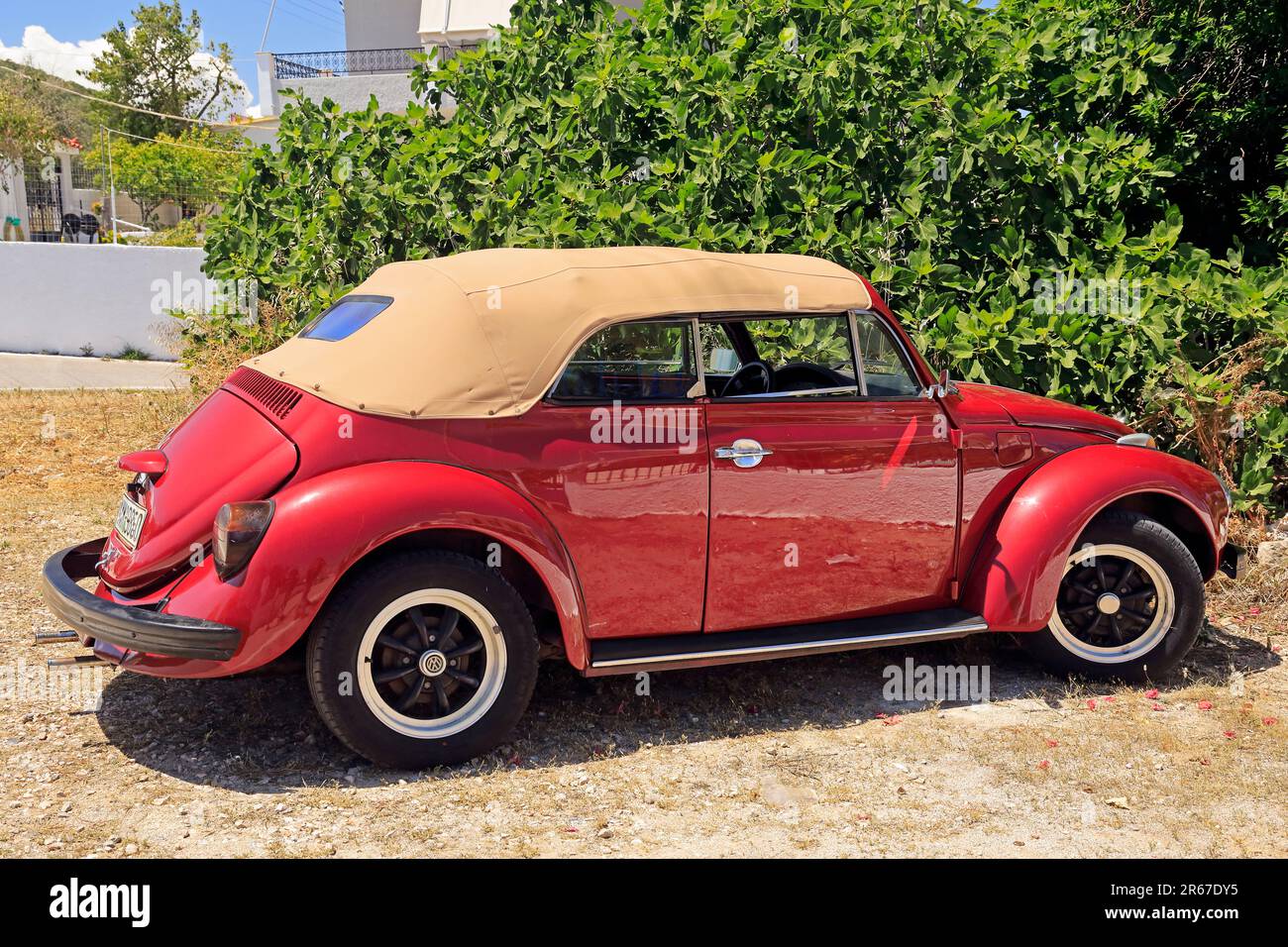 Shiny red well-kept VW Beetle convertible motor car with beige roof parked by the roadside, Agistri island, Saronic Gulf, Greece. May 2023. Stock Photo