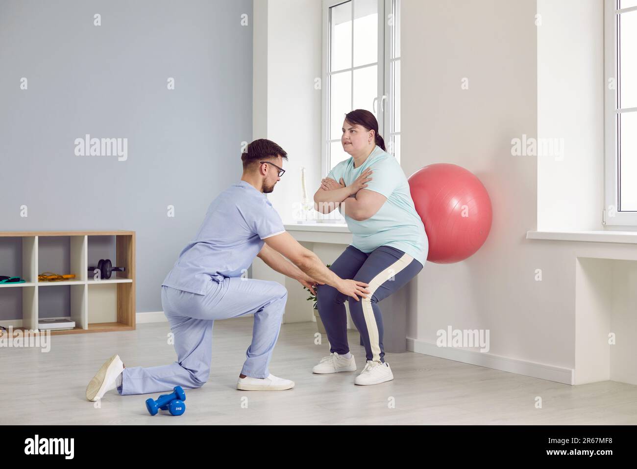 Young male nurse helping fat overweight woman doing sport exercises with fit ball. Stock Photo