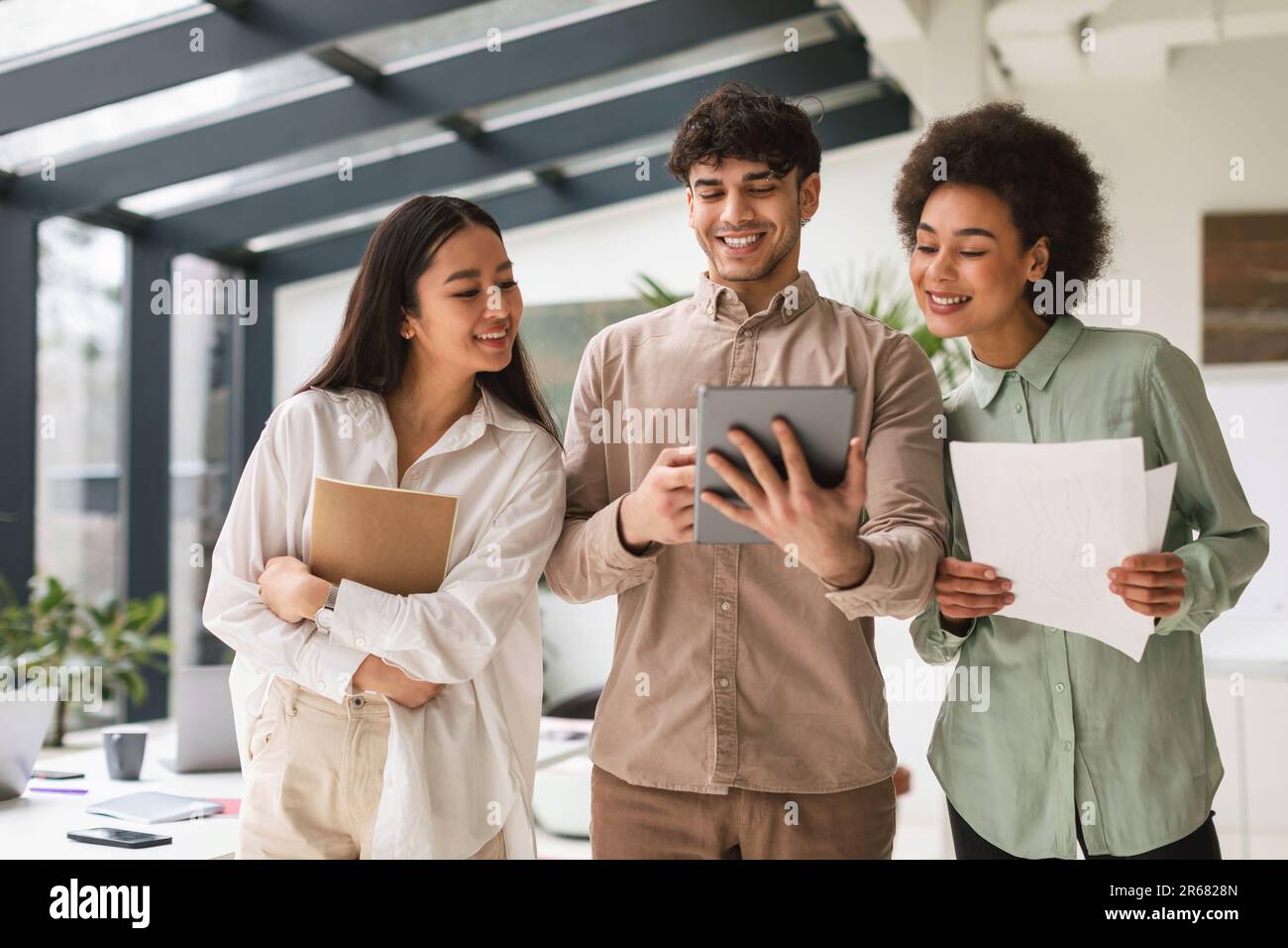 Three Young Multiracial Colleagues Using Tablet Computer Together In Office Stock Photo