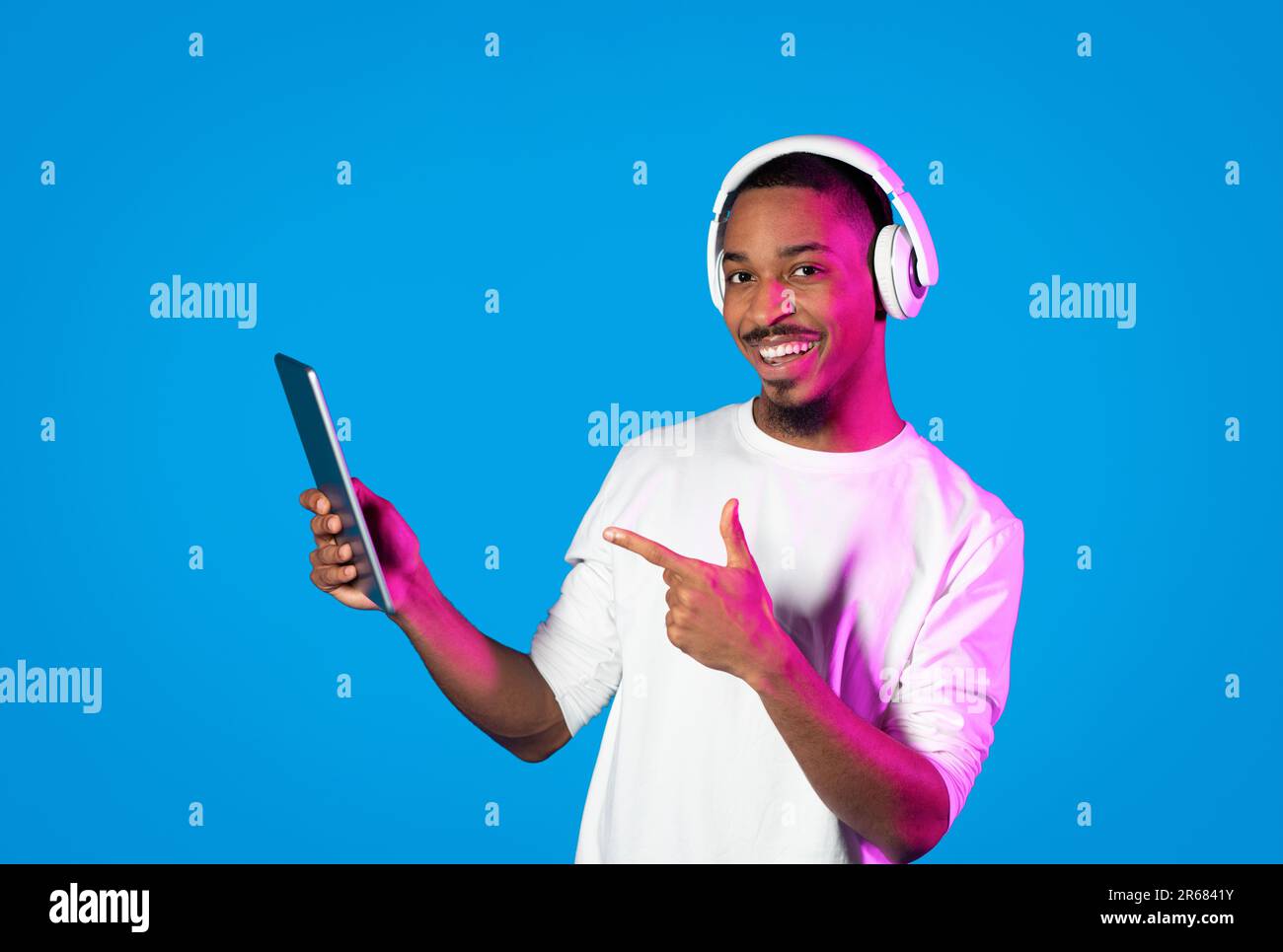 Positive black guy pointing at digital tablet, using headphones Stock Photo