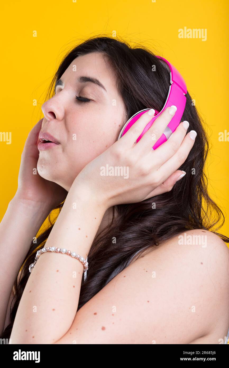 Young woman, wearing pink headphones, savours the engulfing sounds of music, storytelling, on a colorful background Stock Photo