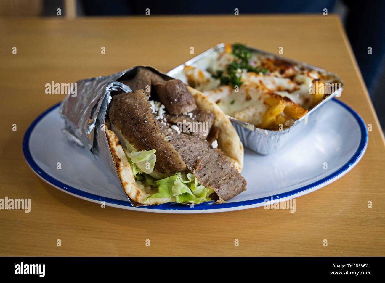 A Greek Mediterranean gyro wrapped in foil on a plate with a side of