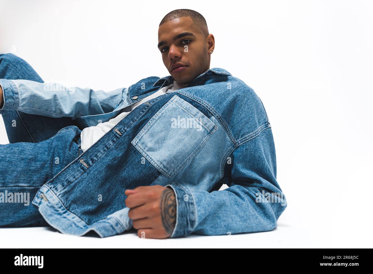 African American man wearing a denim jacket and jeans striking a pose on the floor. Isolated against a white background. High-quality 4k footage Stock Photo