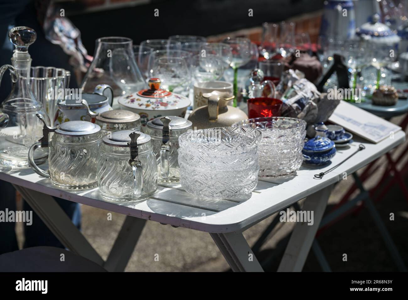 Glass dishes, beer mugs and drinking glasses as well as other tableware on a table at a flea market on a sunny day, selected focus, narrow depth of fi Stock Photo