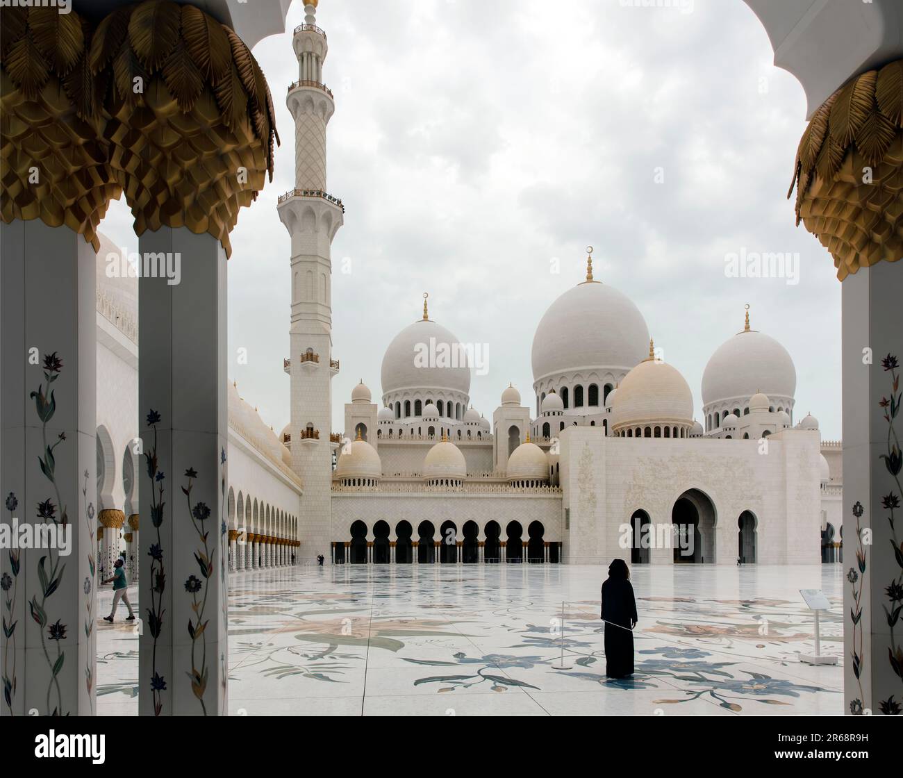 Woman in the central courtyard looks at Minaret and domes of the Sheikh Zayed Grand Mosque, Abu Dhabi UAE viewed through arch Stock Photo
