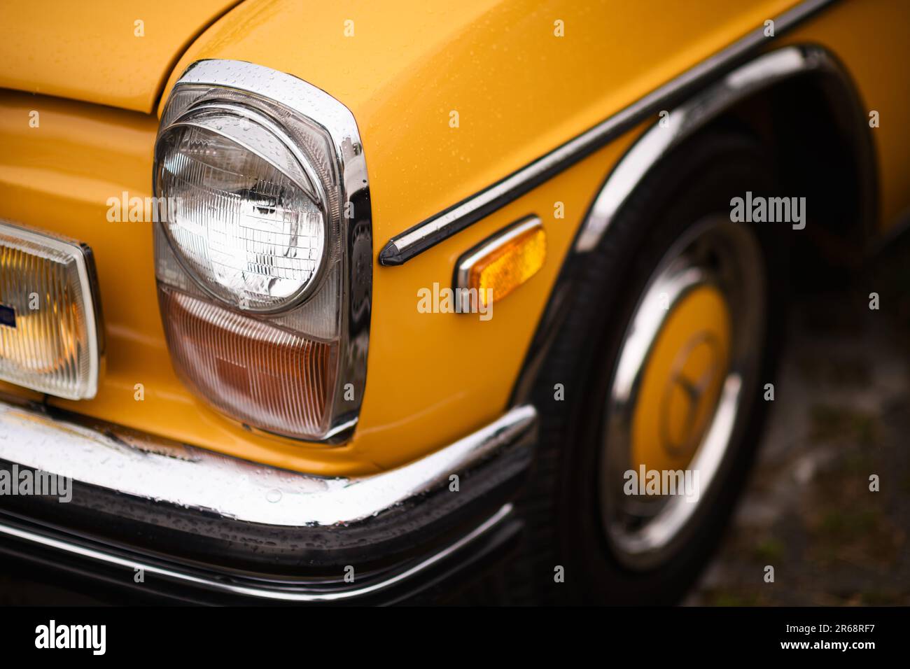 Izmir, Turkey - June 3, 2023: Close-up shot of the headlight on a yellow 1970 Mercedes, covered in raindrops, at the IZKOD Classic Car Meet at Buca Po Stock Photo