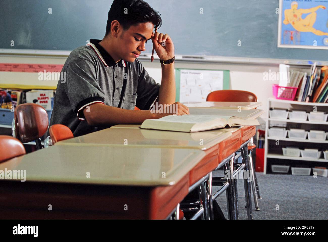 A Latino High school student studying alone at his desk with an open textbook Stock Photo