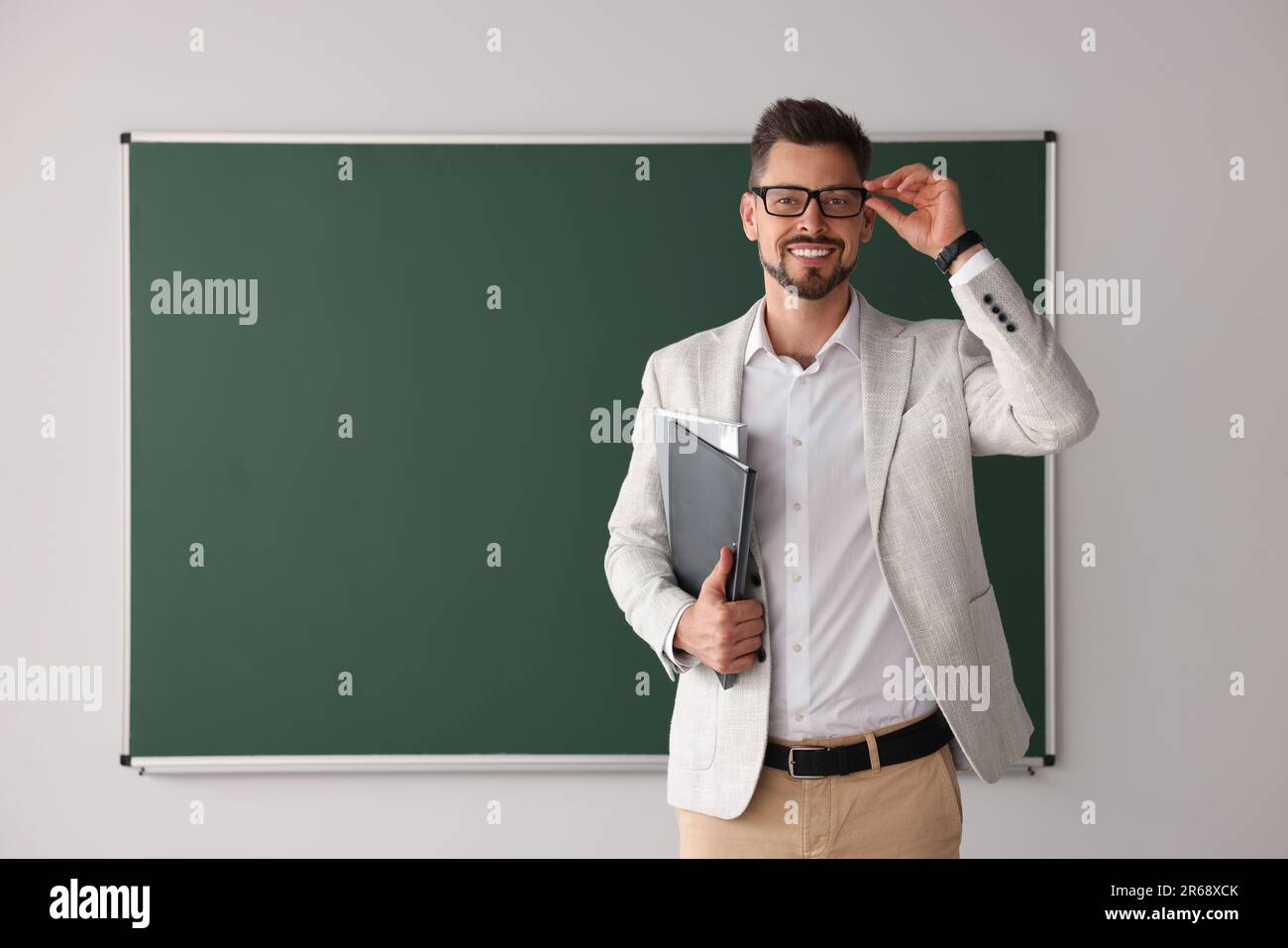 Happy teacher with glasses and stationery at blackboard in classroom ...