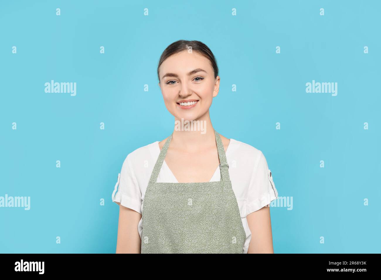 Beautiful young woman in clean apron with pattern on light blue ...