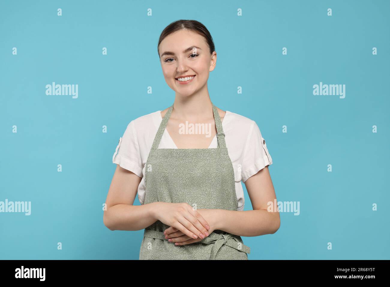 Beautiful young woman in clean apron with pattern on light blue ...