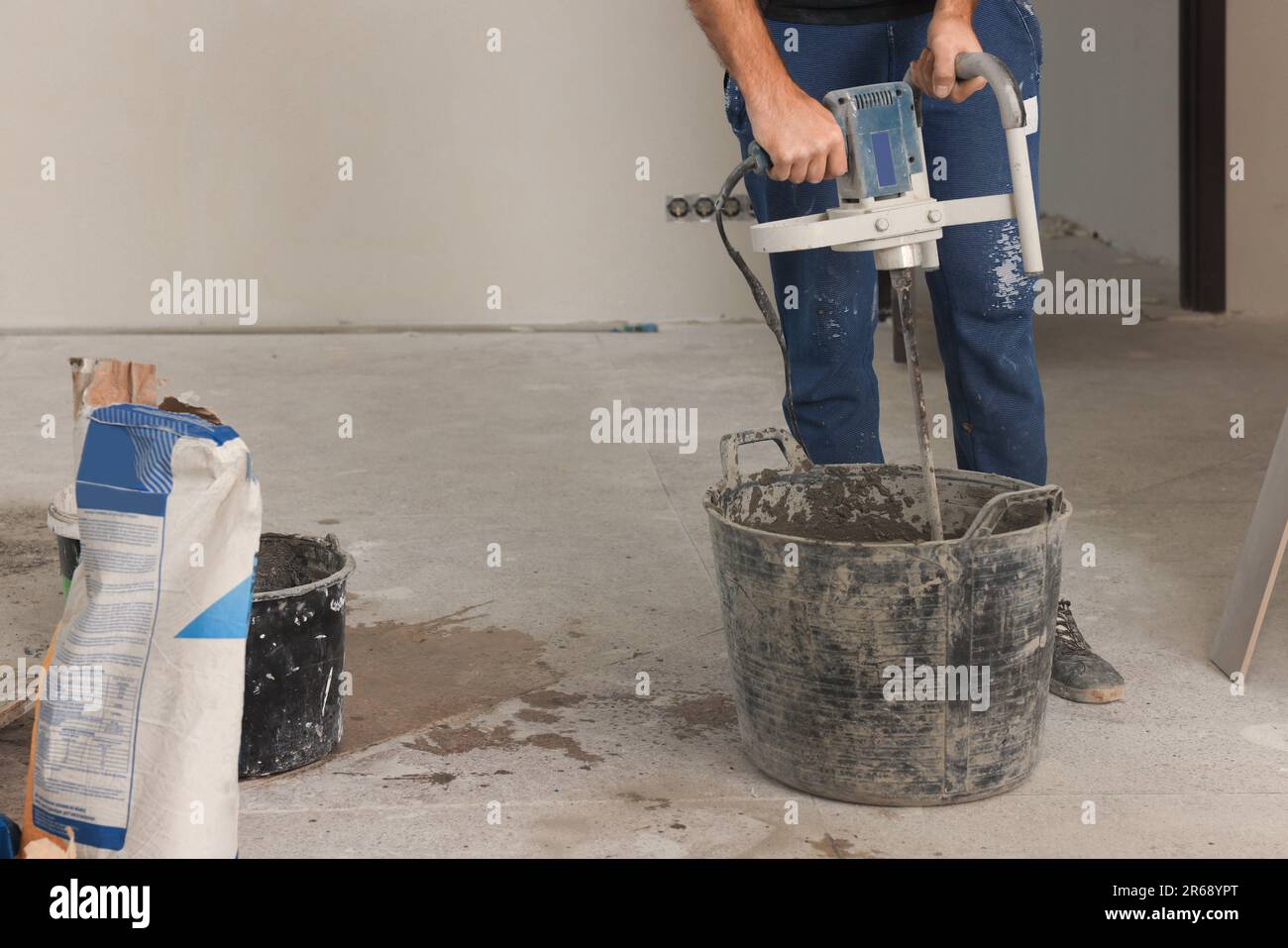 Professional worker mixing cement in bucket indoors, closeup. Tiles