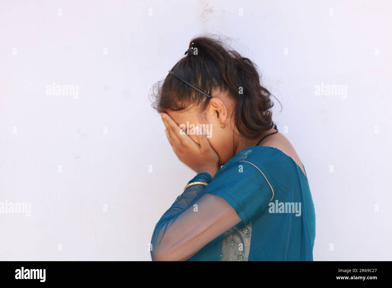 Portrait of a smiling Asian Indian Girl standing and looking at camera isolated over white background. Covering his face with his hands. Stock Photo