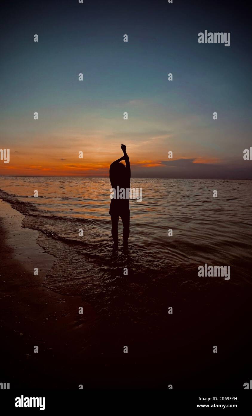 A silhouette of a female figure standing on the beach at sunset Stock ...