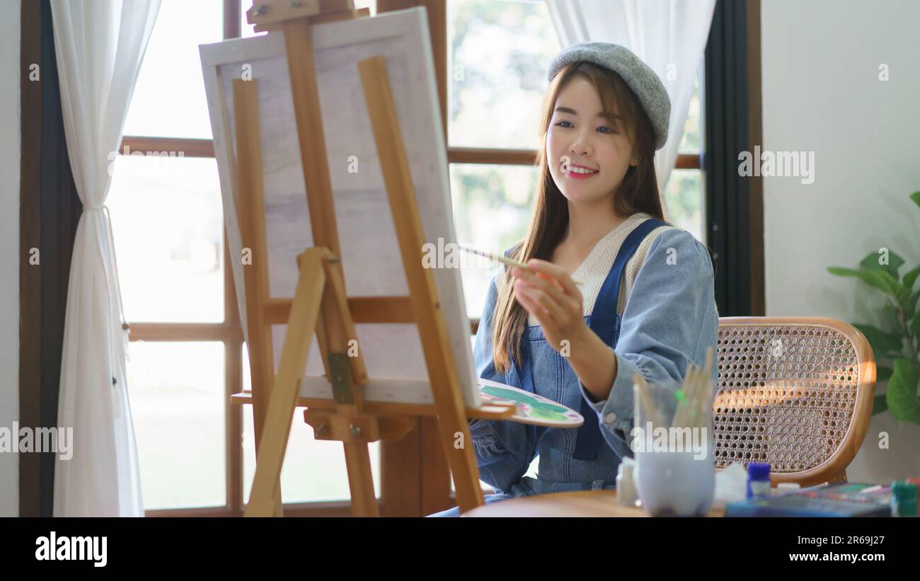 Young female painter holds color palette and use brush to painting ...