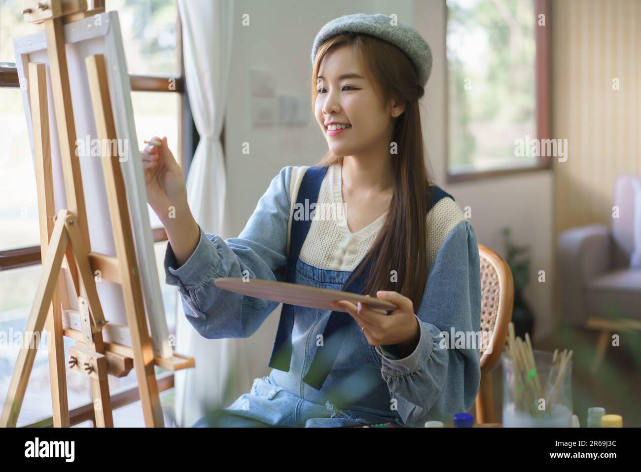 Young female artist holds color palette and use brush to painting ...