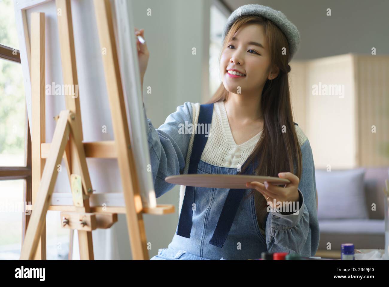 Young female artist holds color palette and use brush to painting ...