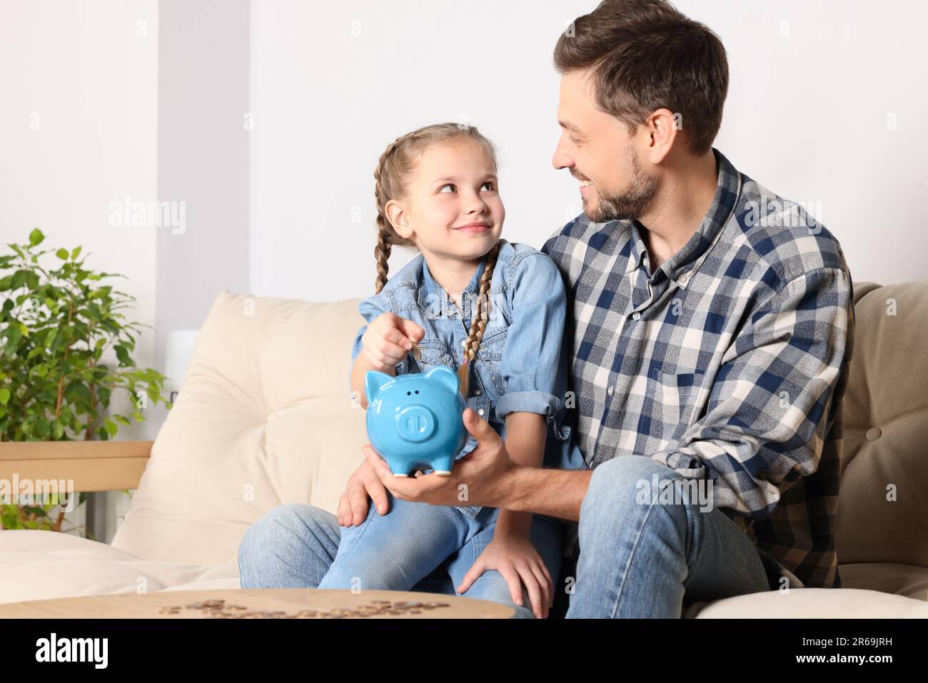 Little girl with her father putting coin into piggy bank at home Stock ...