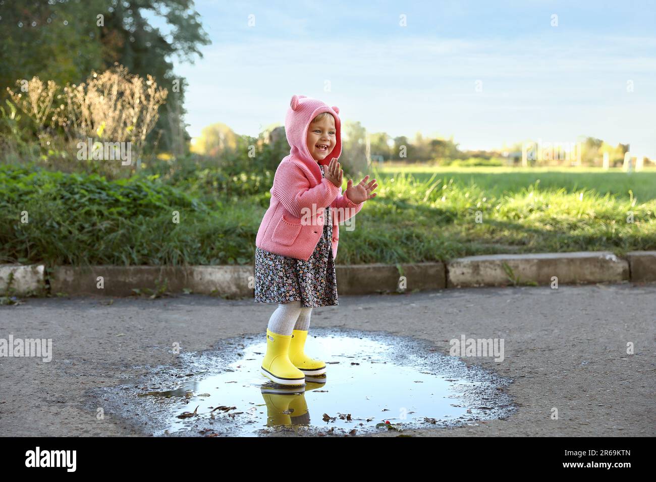 Little girl wearing rubber boots standing in puddle outdoors. Autumn ...