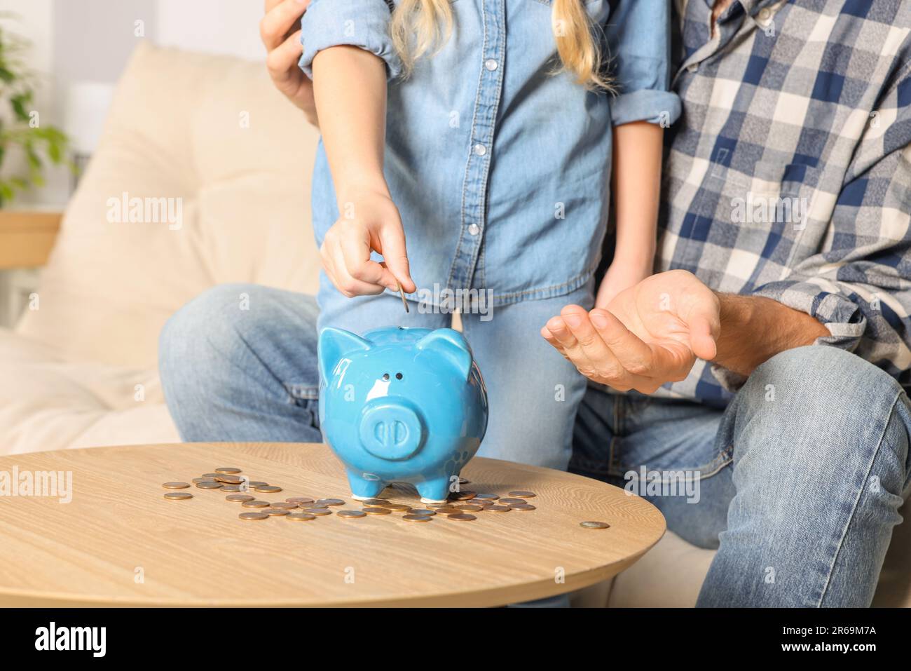 Little girl with her father putting coin into piggy bank at home ...