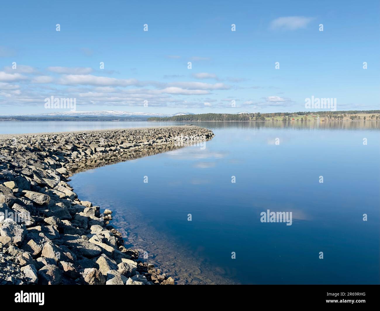 Tranquil lakeside scene with a stone jetty under a bright blue sky Stock Photo