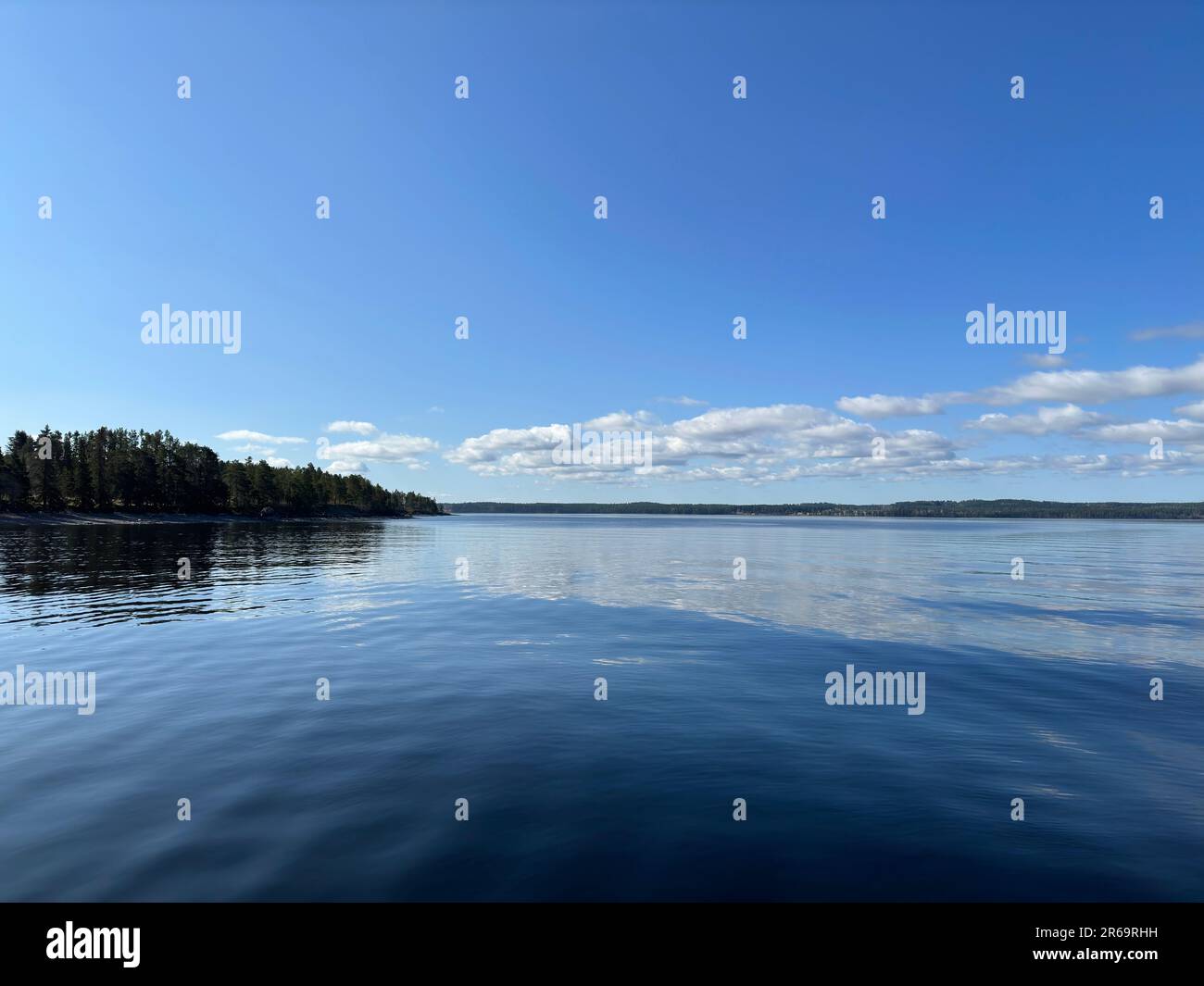 The calm lake under a clear blue sky with puffy white clouds on a ...