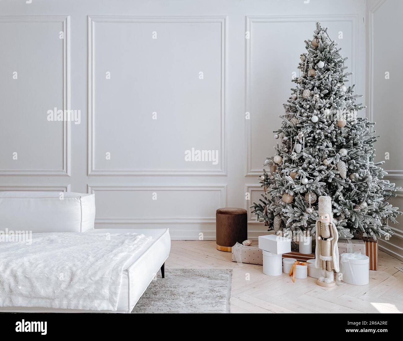 Studio decorations with stylish decorated Christmas tree with presents, toys, nutcracker in big white spacious living room with modern interior, sofa Stock Photo