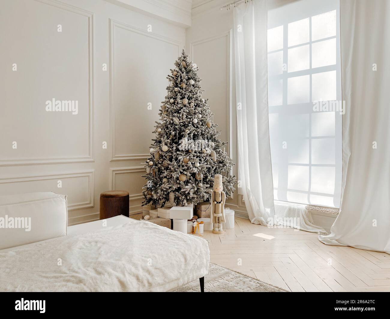 Studio decorations with stylish decorated Christmas tree with presents, toys, nutcracker next to big windows in white spacious living room with Stock Photo