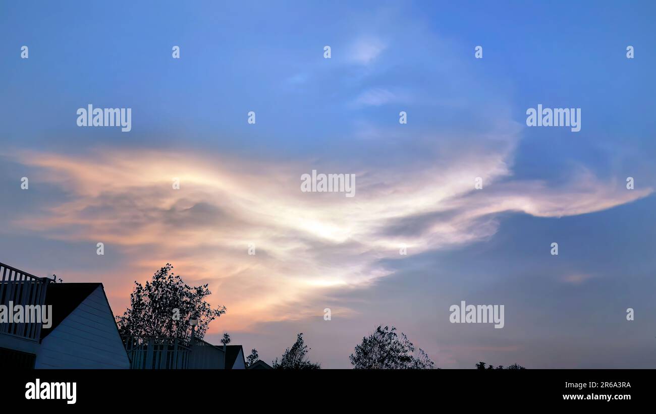 Sunset in the evening with dramatic shape and color of clouds and sky with Silhouette of housing and trees, skyline, cloudscape, nature background Stock Photo