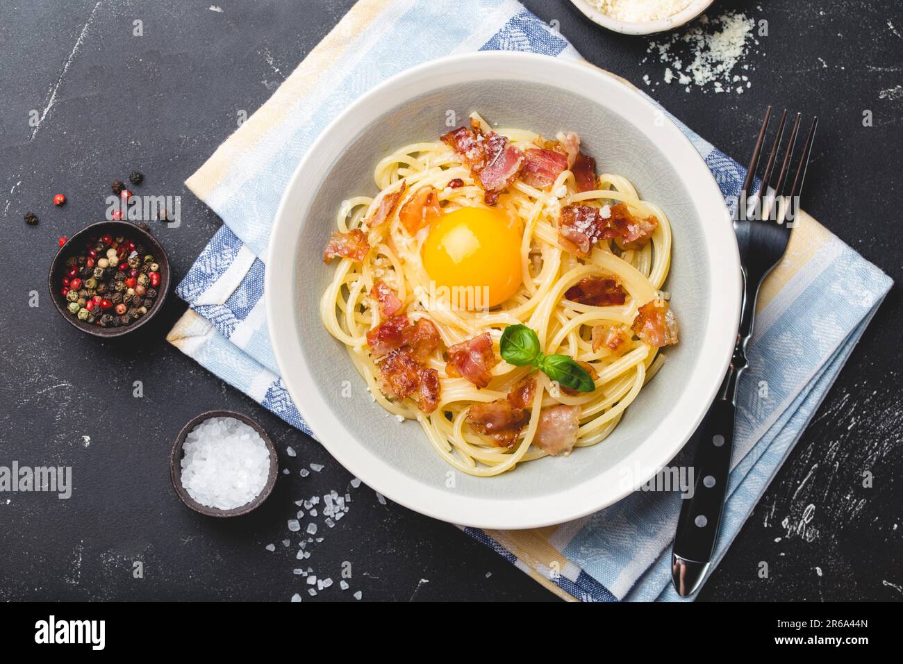 Traditional Italian pasta dish, spaghetti carbonara with yolk, parmesan cheese, bacon in plate on black rustic stone background, top view. Italian Stock Photo