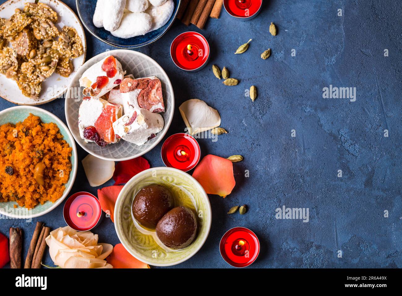 Indian Diwali celebratory background with traditional sweets. Gulab jamun, carrot halwa, snacks with candles, flowers. Assorted indian desserts. Stock Photo