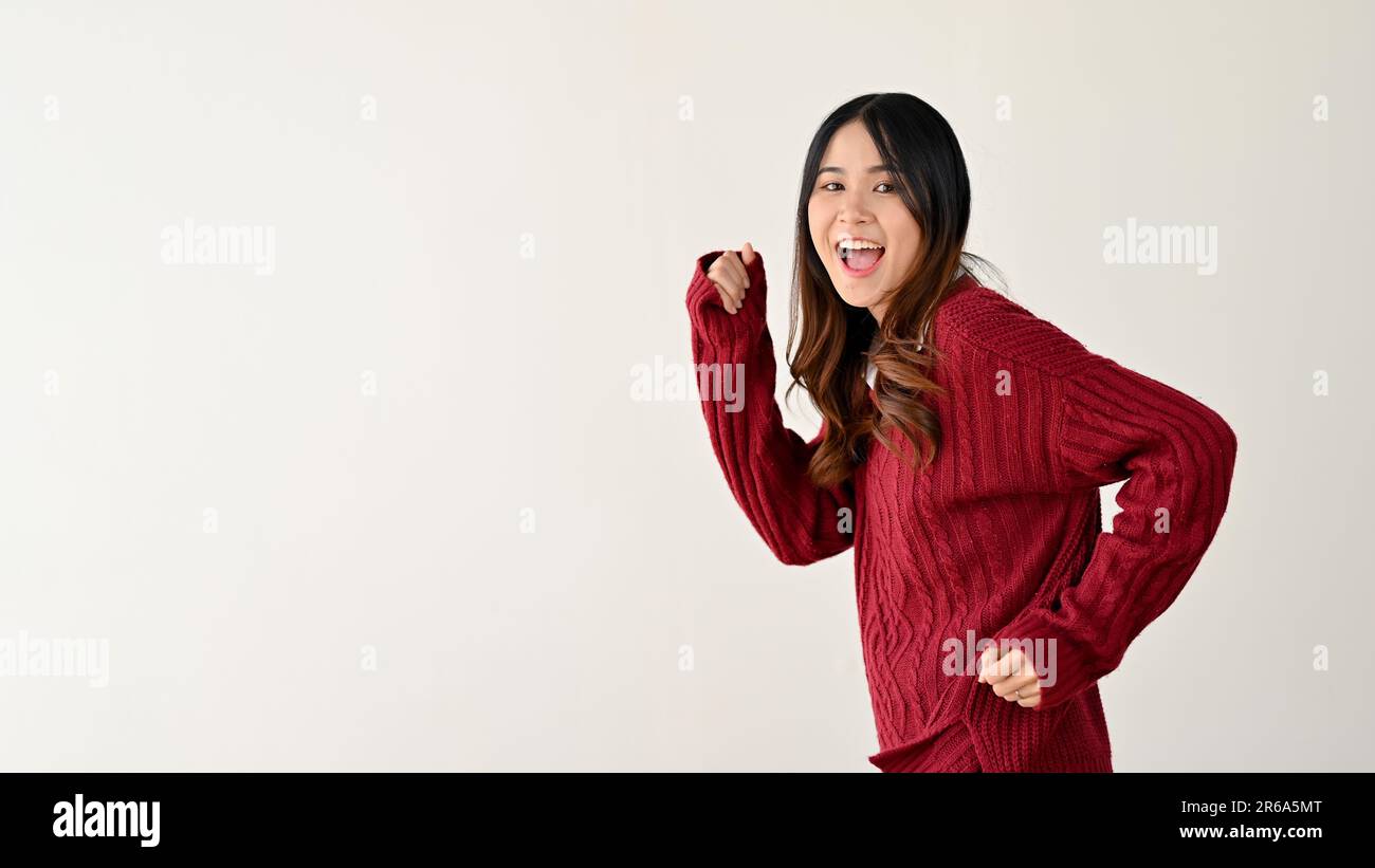 A cheerful and positive young Asian woman in a red sweater with running posture, copy space on an isolated white background. hurry up, hot deal, quick Stock Photo