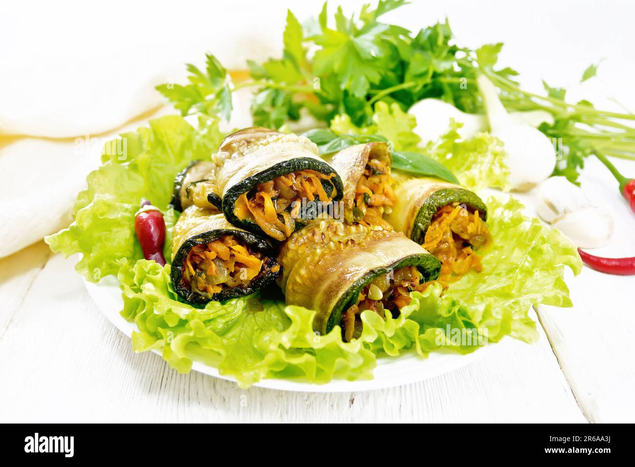 Spicy appetizer of zucchini with carrots, onions and garlic on lettuce leaves in a plate, napkin, hot peppers on white wooden board background Stock Photo