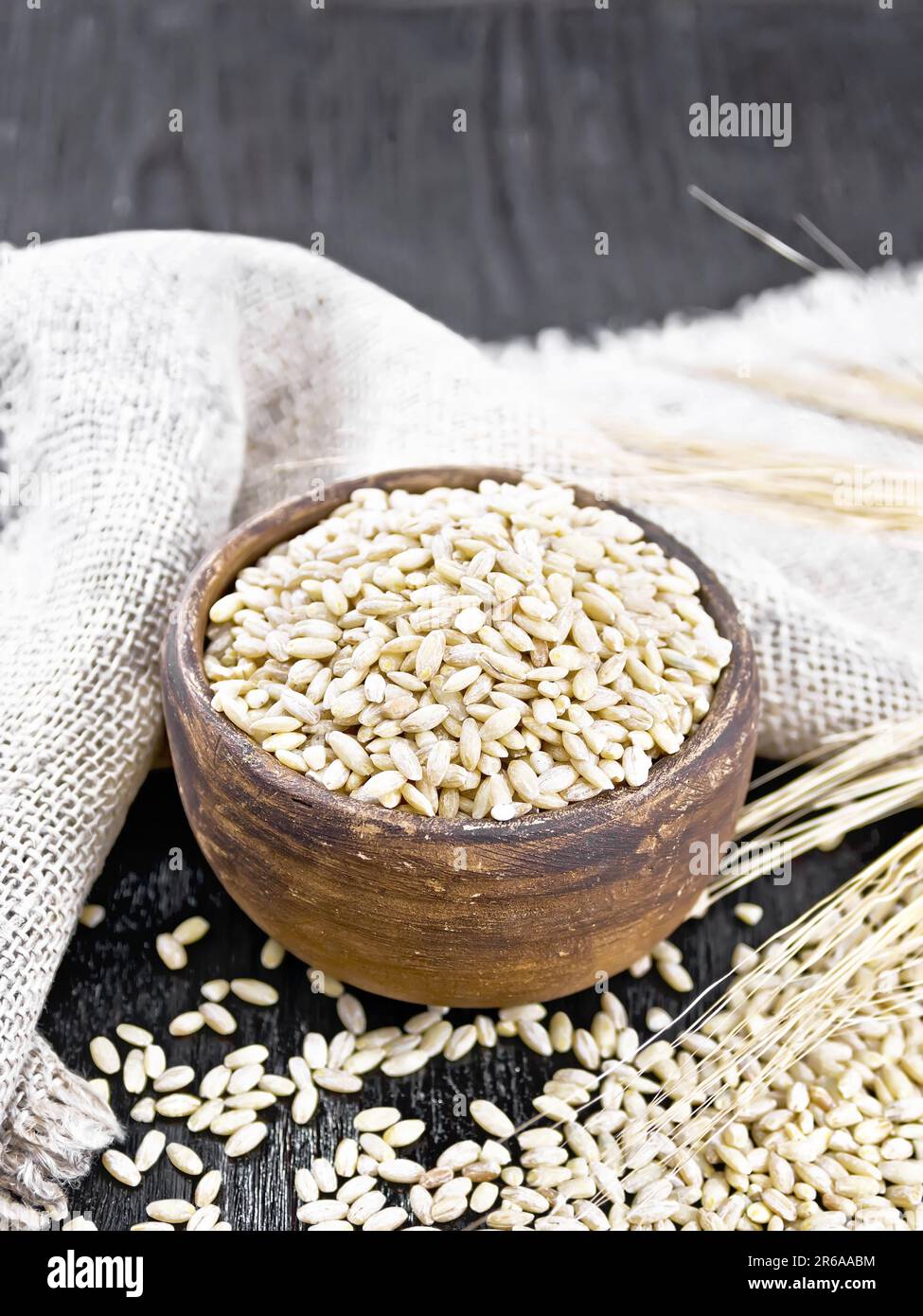 Spelled in a bowl and on the table, stalks with ears of wheat, burlap on the background of wooden board Stock Photo