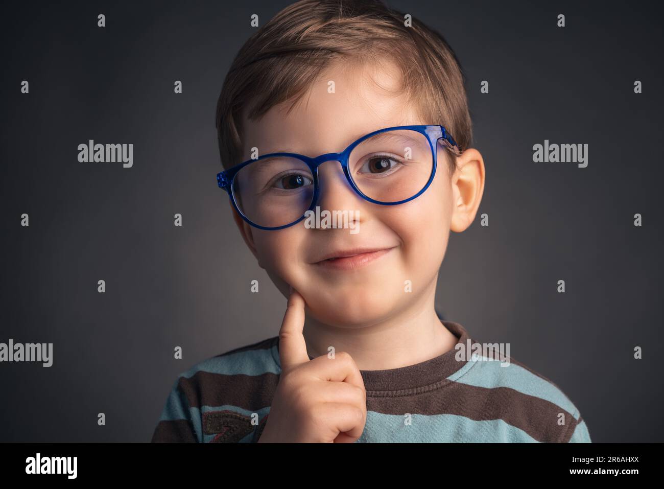 Cute, smile, funny and clever, little boy with glasses, studio portrait on black background. Smart preschooler. Stock Photo