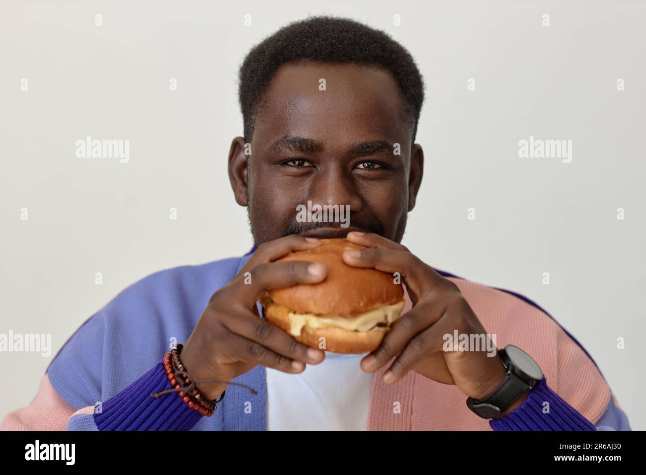 Front view portrait of young black man eating takeout burger and looking at camera against white Stock Photo