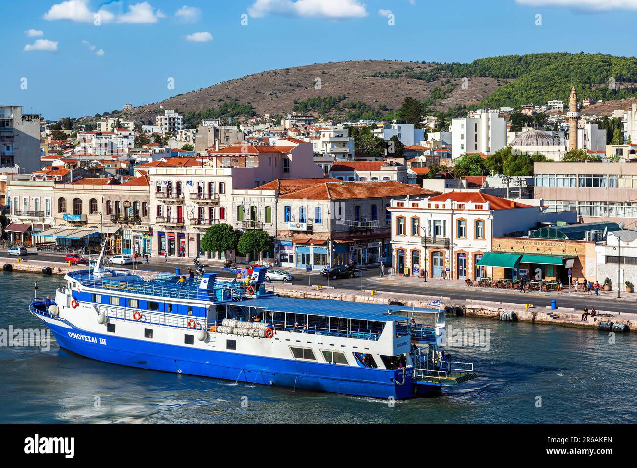 View of Chios town and port, as seen from aboard a vessel. A blue touristic ship has just set sails, as it happens during the summer season. Stock Photo