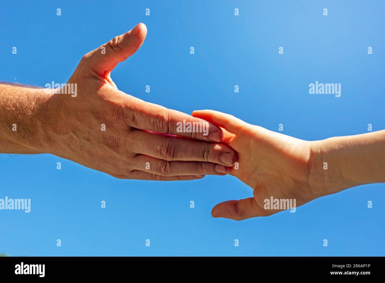man's hand touches the child's palm against the background of the blue sky. Help the girl Stock Photo
