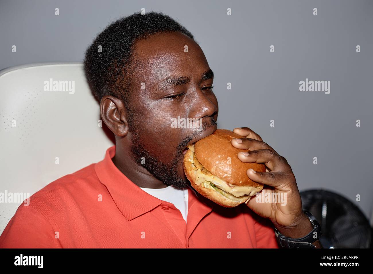 Minimal side view portrait of black man eating burger indoors shot with flash, copy space Stock Photo