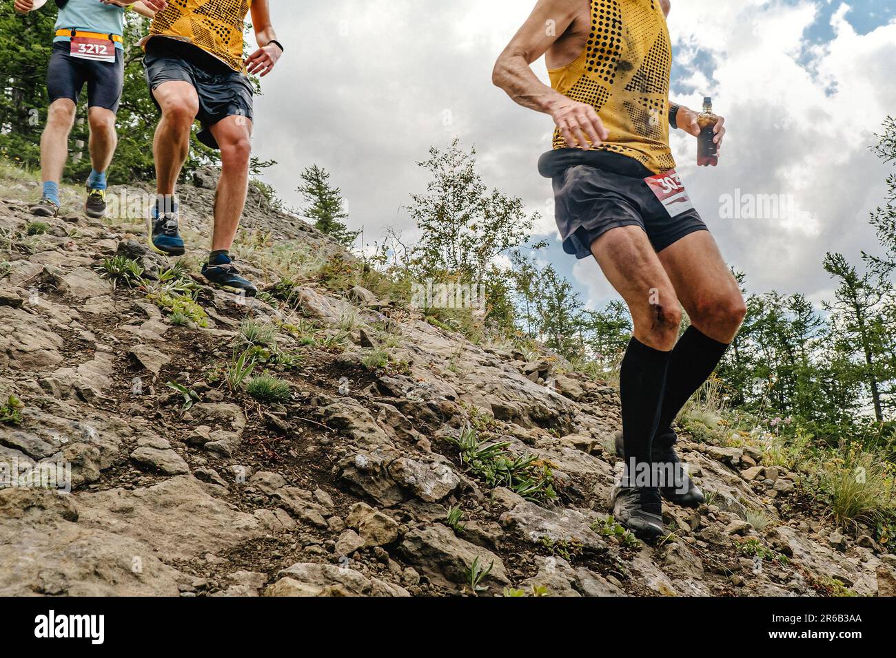 group athletes runners running down steep mountainside, summer trail marathon race Stock Photo